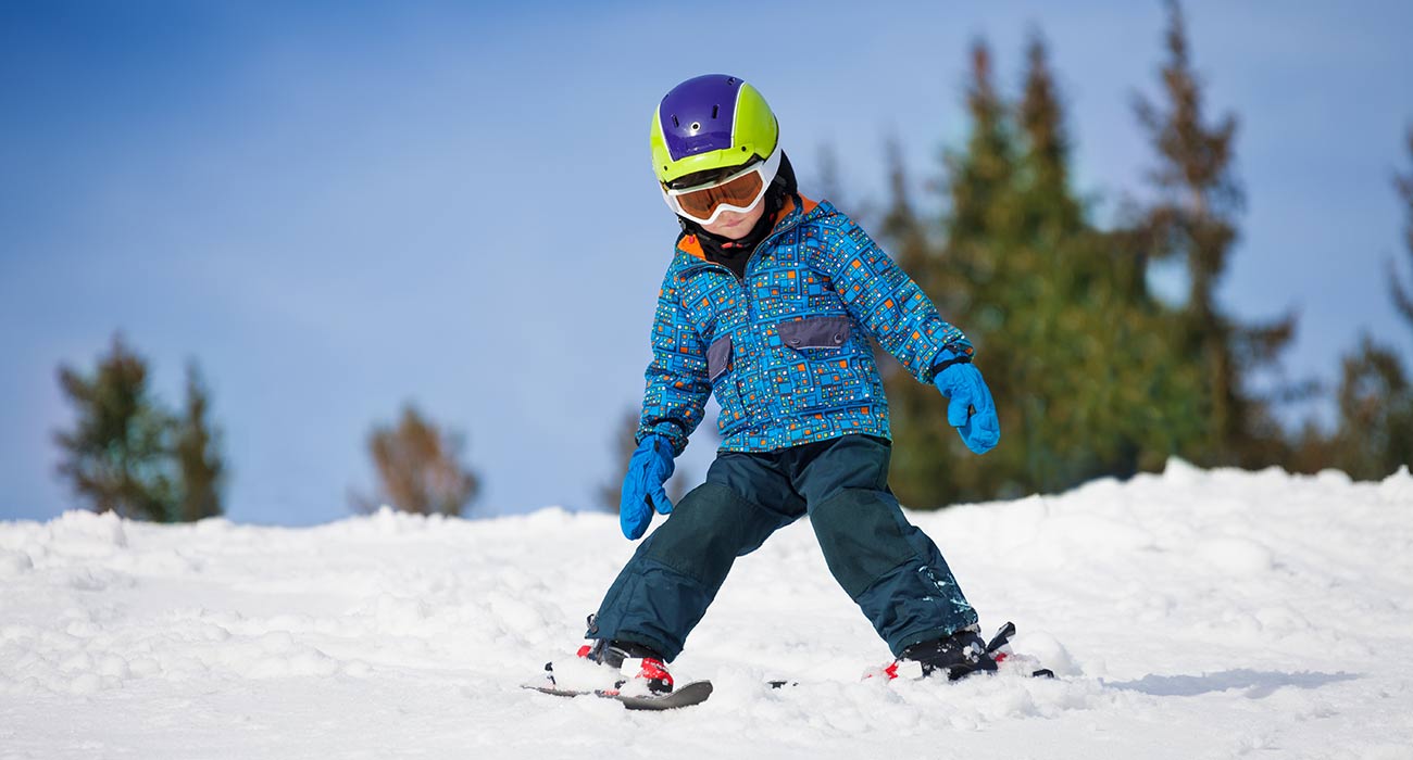 Bambino sugli sci con casco e occhiali scende dalla pista